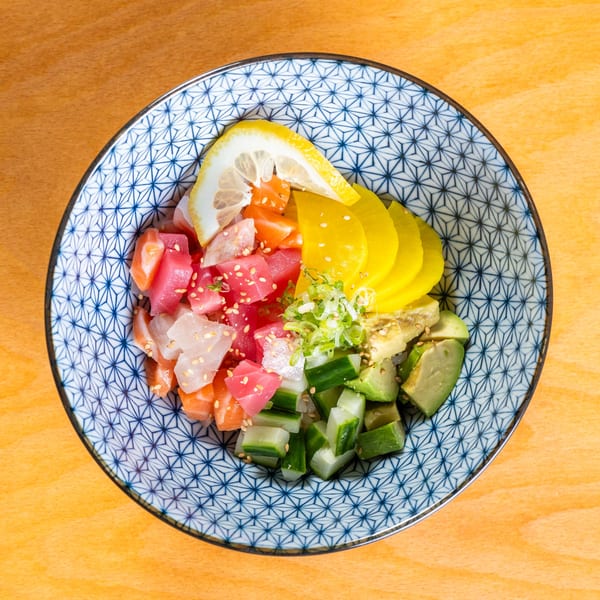 Colorful poke bowl with tuna, salmon, avocado, cucumber, pickled radish, and lemon in a patterned bowl.