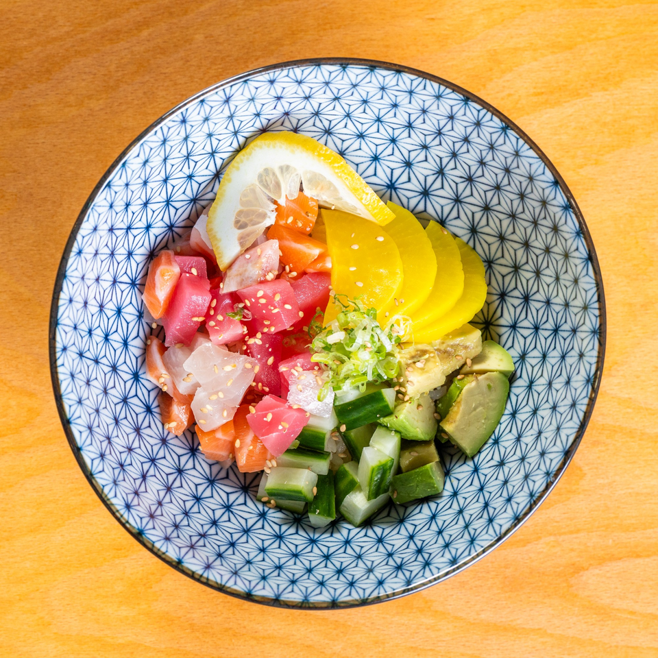 Colorful poke bowl with tuna, salmon, avocado, cucumber, pickled radish, and lemon in a patterned bowl.