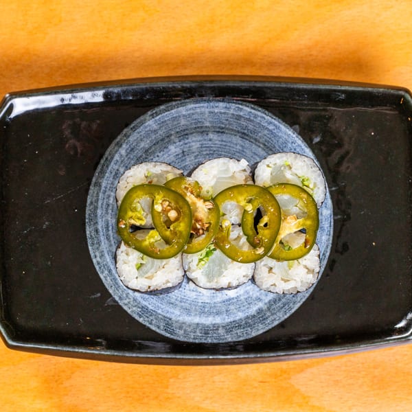 Six sushi rolls topped with sliced green jalapeños on a black and grey plate.