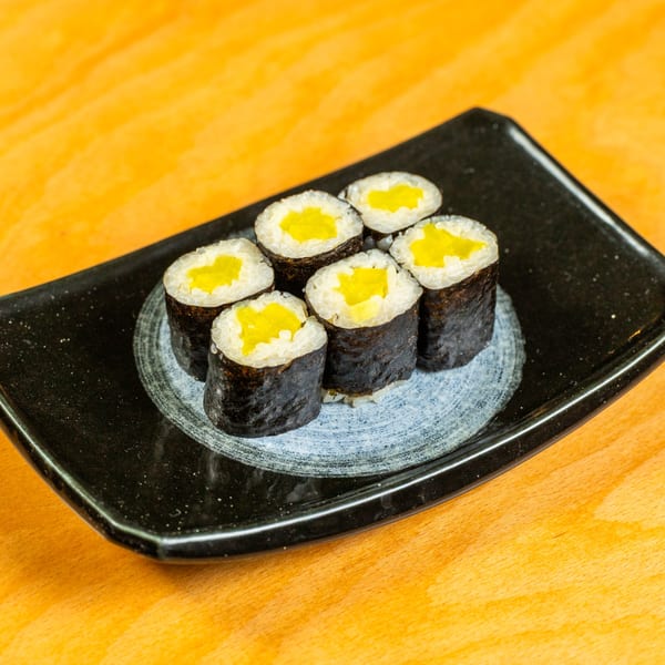 Six pieces of yellow pickled radish sushi rolls on a black rectangular plate.