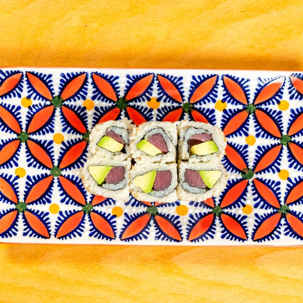 Six pieces of tuna and avocado sushi rolls on a colorful patterned rectangular plate.