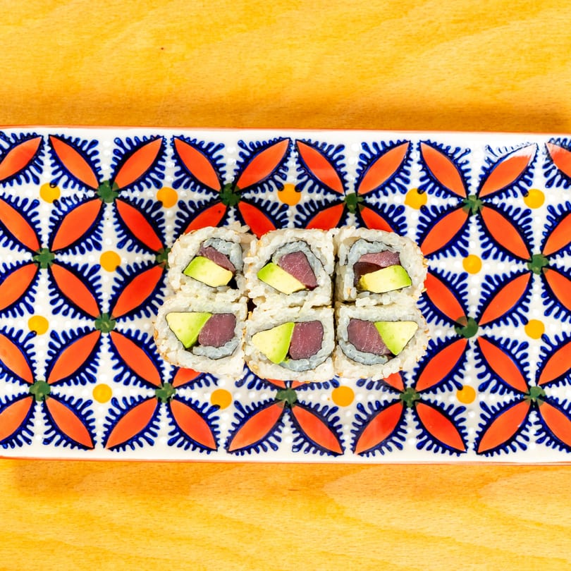 Six pieces of tuna and avocado sushi rolls on a colorful patterned rectangular plate.