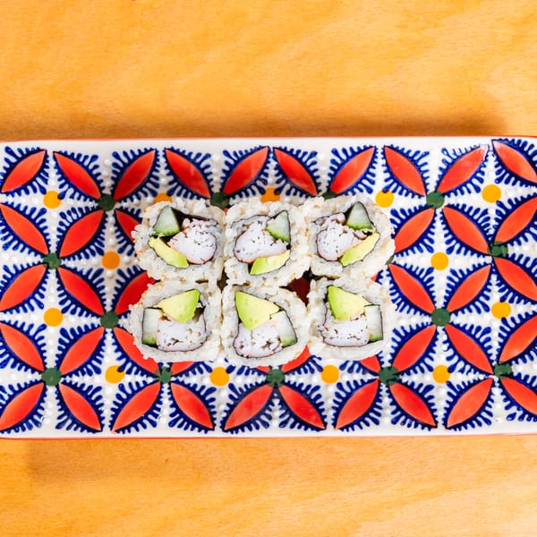 Six California sushi rolls with avocado, crab, and cucumber on a colorful patterned plate.