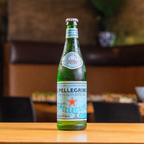 A chilled green glass bottle of San Pellegrino sparkling water stands on a wooden table.