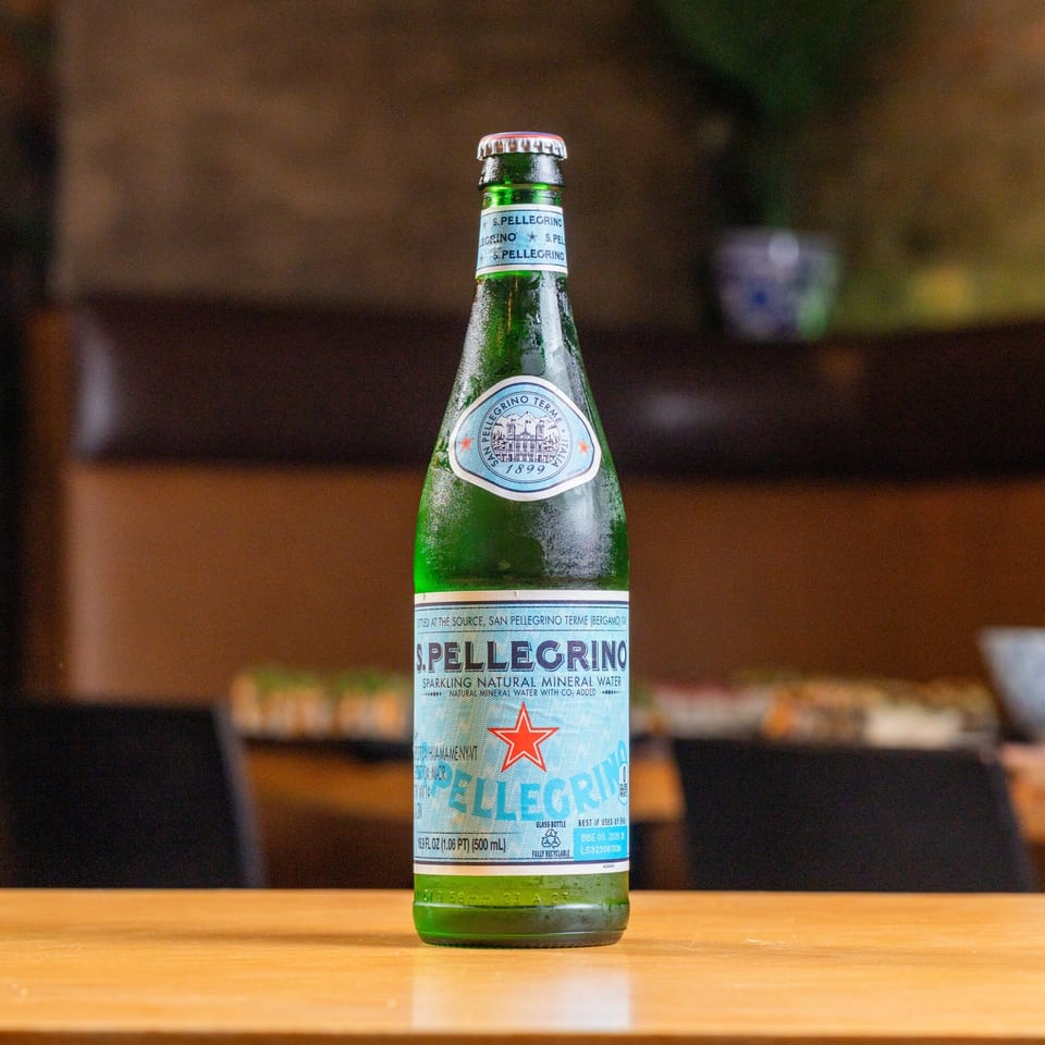 A chilled green glass bottle of San Pellegrino sparkling water stands on a wooden table.