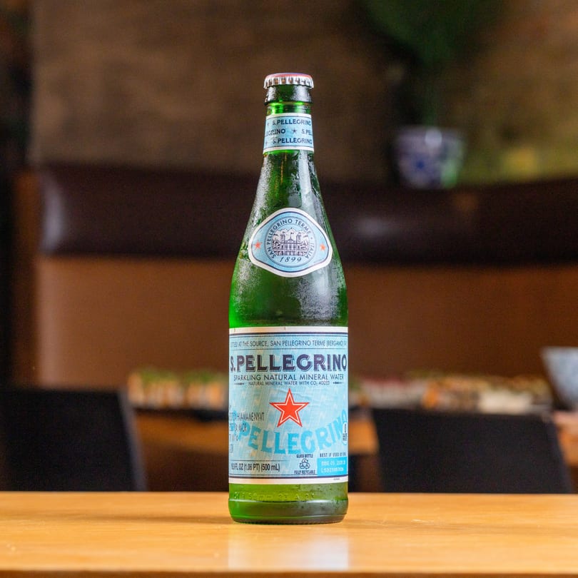 A chilled green glass bottle of San Pellegrino sparkling water stands on a wooden table.