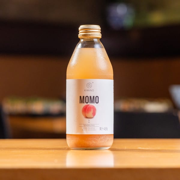 A chilled bottle of Kimino Momo sparkling peach juice with a white label sits on a wooden table.