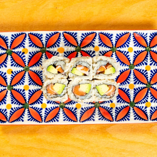 Six pieces of salmon and avocado sushi rolls on a colorful patterned rectangular plate.