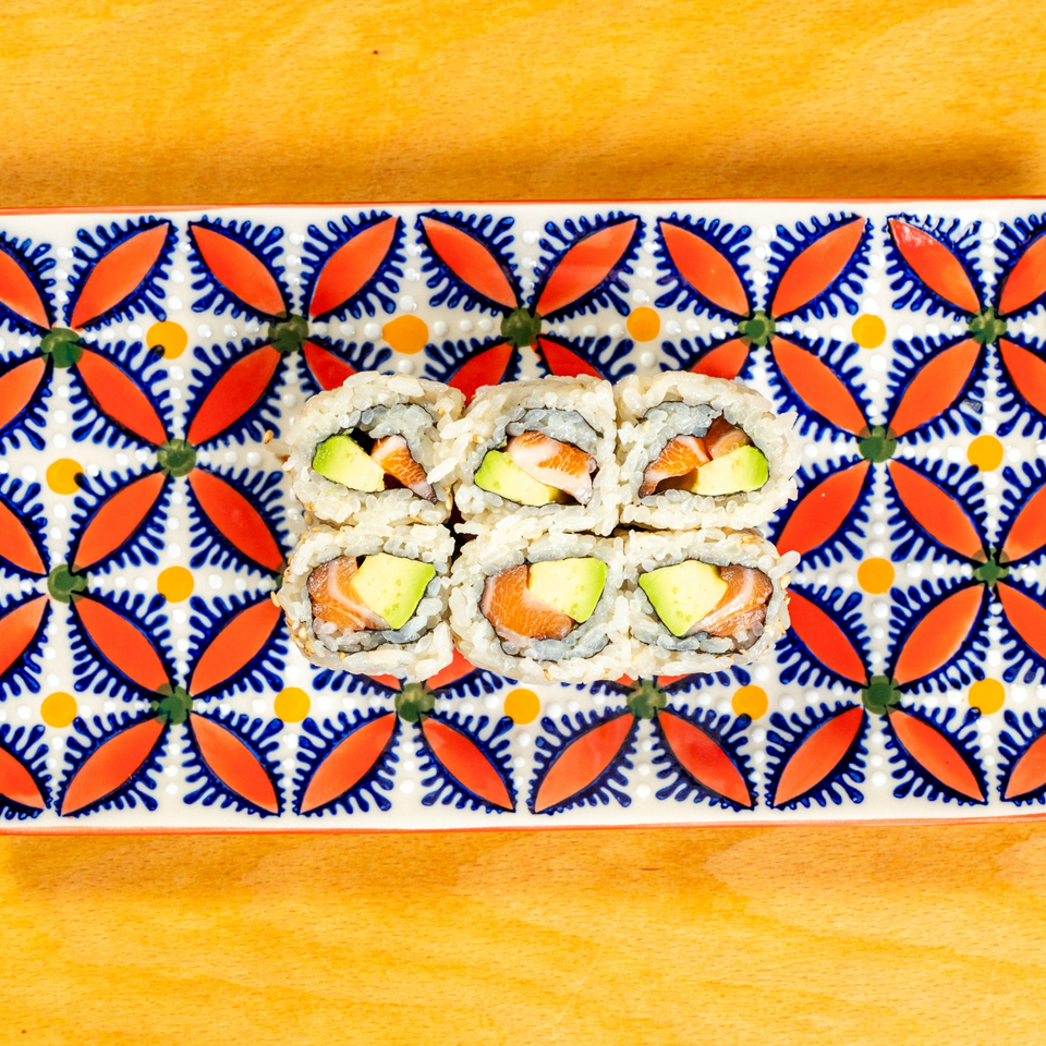 Six pieces of salmon and avocado sushi rolls on a colorful patterned rectangular plate.