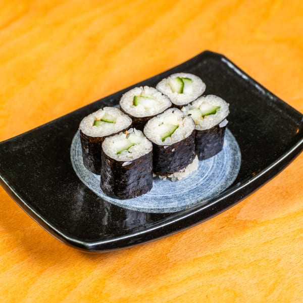 Six cucumber maki sushi rolls with white rice and nori, served on a black rectangular plate.